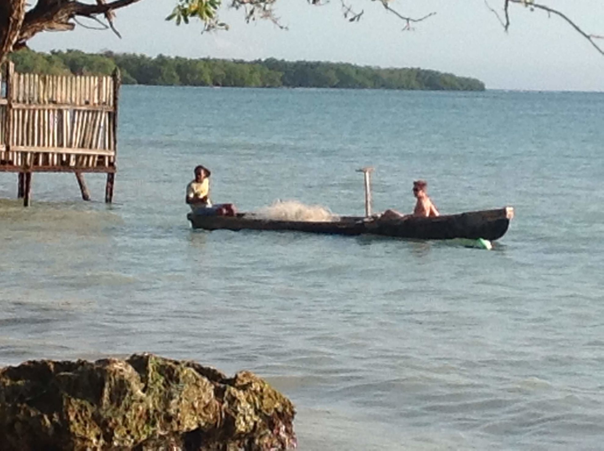 Two people sit in a canoe near a dock on the sea.
